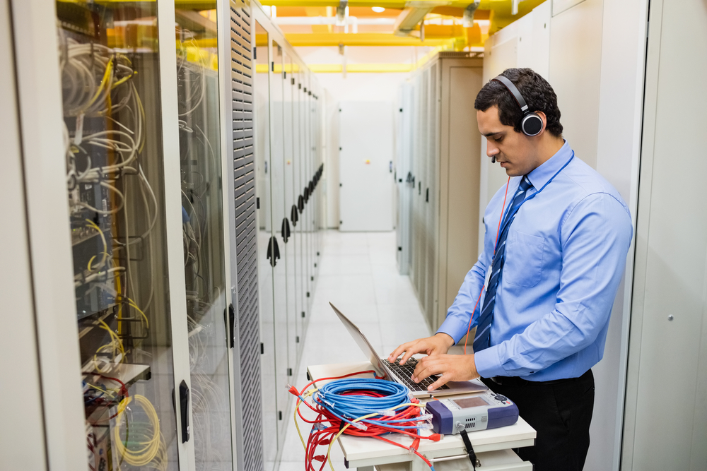 Technician In Head Phones Using Laptop In Server Room